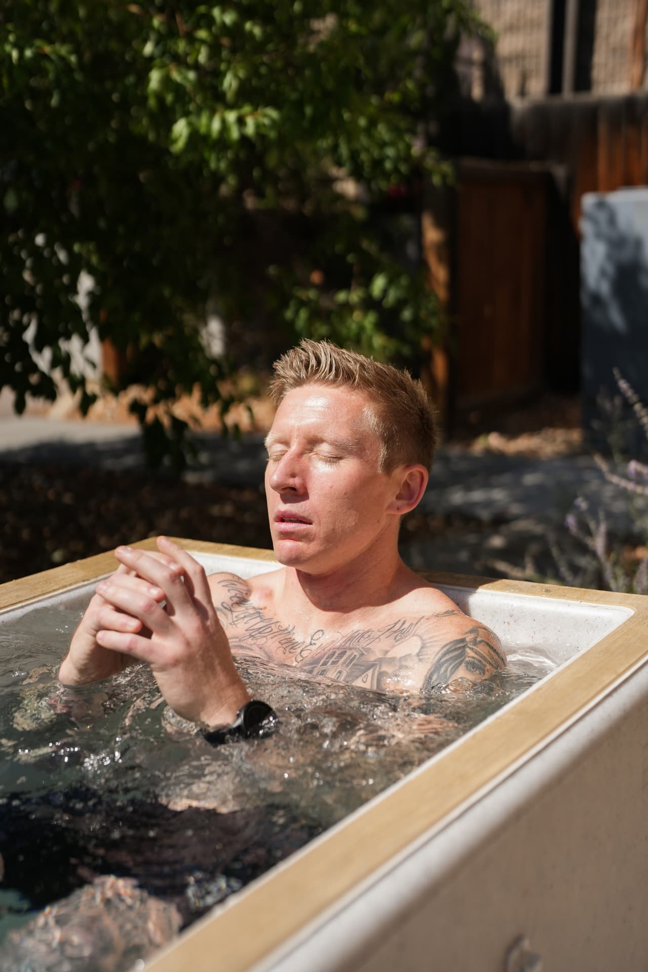Man sitting in an outdoor cold plunge tub with his eyes closed and hands clasped, breathing through the cold.