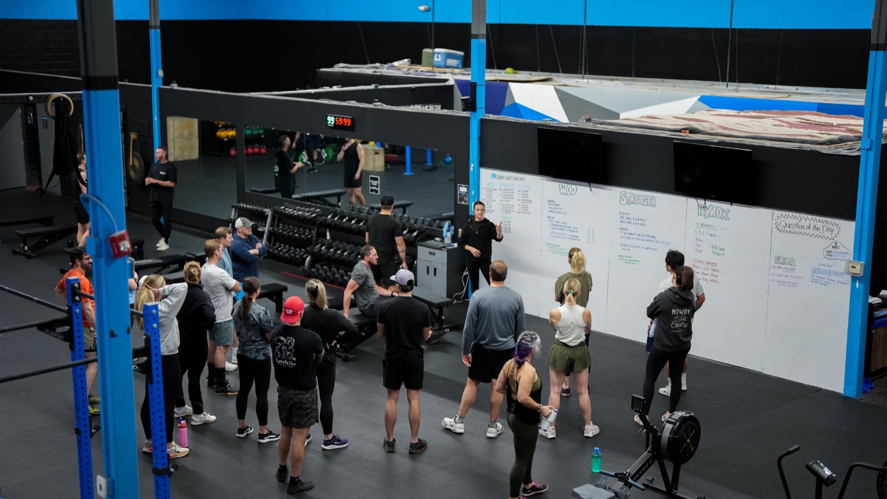 Group of members gathered around a coach in front of the whiteboard before a class at the Arsenal Health gym.